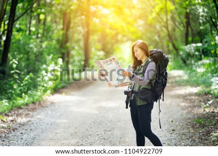 Hipster Asian young girl with backpack enjoying forest on mountain.Tourist traveler with trendy look searching direction on location map , Greenfield. Hiker looking sunlight in trip in the countryside