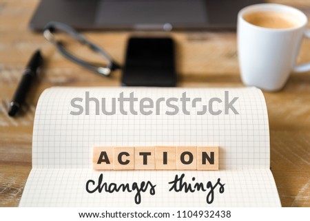 Closeup on notebook over wood table background, focus on wooden blocks with letters making Action Changes Things text. Concept image. Laptop, glasses, pen and mobile phone in defocused background