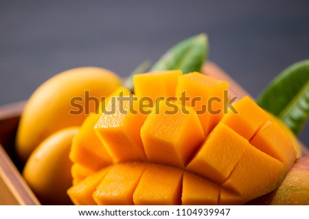 Fresh and beautiful mango fruit set in a wooden box with sliced diced mango chunks on a dark wooden background, copy space(text space), blank for text Royalty-Free Stock Photo #1104939947