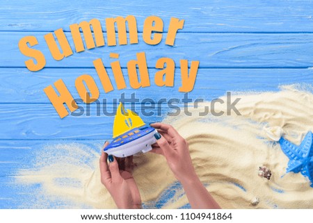 Female hands with toy boat by Summer holiday inscription on blue wooden background
