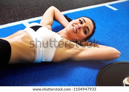 Sporty girl is laying on a blue colored floor in the gym resting and smiling