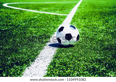 A soccer ball in near the corner marking of a football field on green grass.