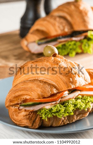 Photo of tasty and fresh croissant sandwich with salad, ham, cheese, tomatoes on wooden background. Morning breakfast concept. Healthy and fast food.