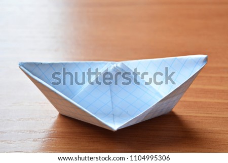 Origami a paper boat from a white empty blank sheet in a cell on wooden table.