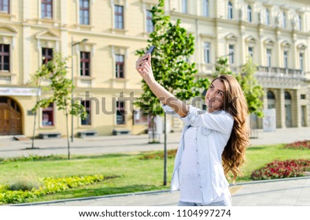 Beautiful young brunette with long hair taking smiling selfi in the town