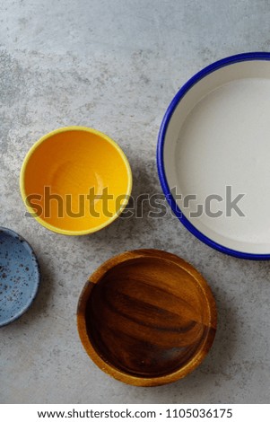 Overhead image of various plates and bowls made of different materials placed on metallic background