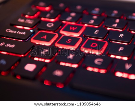 Black gaming keyboard with red backlight, focus on WSAD control keys, blurry close up 