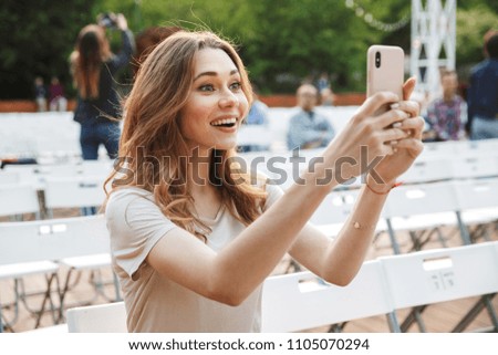 Excited young girl taking picture with mobile phone while sitting on a chair at the park