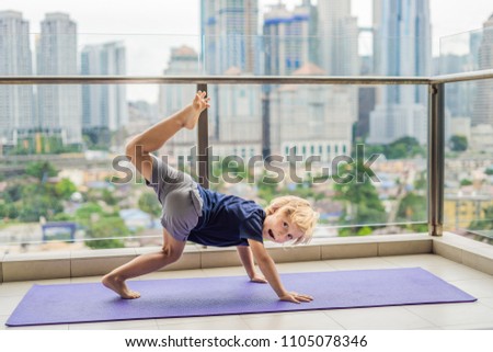 Happy little boy is practicing yoga on his balcony with a panoramic view of the big city.