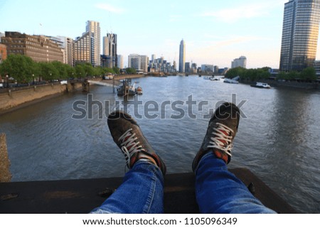 POV image of legs as the photographer sits on a high vantage point looking out at the Tames River in London, England.
