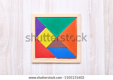 A tangram puzzle consisting of colored pieces with geometric shapes, collected in a square on a light wooden background
