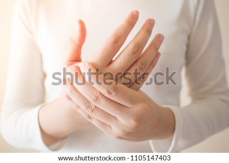Young female in white t-shirt suffering from pain in hands and massaging her painful hands. Causes of hurt include carpal tunnel syndrome, fractures, arthritis or trigger finger. Health care concept. Royalty-Free Stock Photo #1105147403