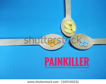 Painkiller word with wooden spoon and pills in the blue paper texture background.