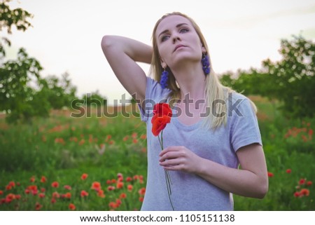 Blonde girl in a field full of poppy flowers. Girl holding poppy flowers. Smiling and dreaming girl. Portraits. Copy space. 