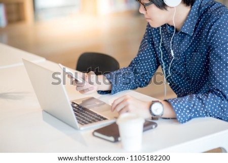 Young Asian businessman dressed in casual style holding smart phone and working with laptop computer on modern desk. Freelance job and IT modern lifestyle, work life balance concept