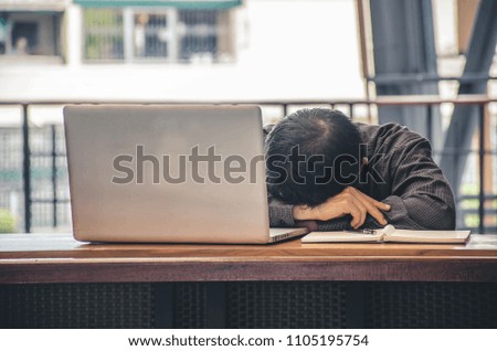 Tired businessman sleeping at his working place office with head on the desk near monitor of computer.