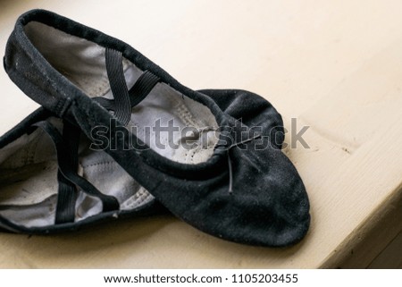 Old ballet shoes isolated on background. Black and worn out training shoes of ballet dancer. Shoes for dancing and training in class. Beige and black background. 