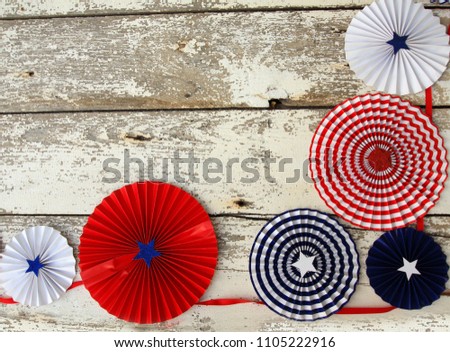 Red white and blue hanging decoration in a boarder. Sitting on a rustic white wooden background. The decorations are circles with stars and  stripes. 