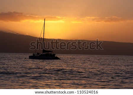 a catamaran silhourtte in the sunset on Maui island in background