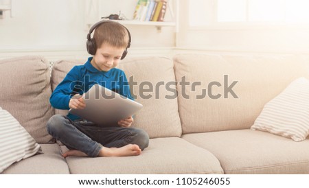 Little boy in headphones playing online game on tablet, having fun at home. Gadgets and technology, success concept, copy space