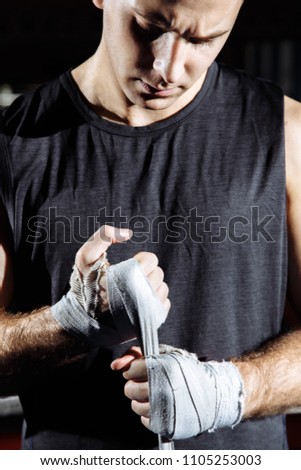 Strong man is wrapping hands with boxing wraps for fight and active exercise in fitness gym