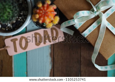 International Father Day concept wrapped craft paper gift box placed on vintage wooden background with blurred cactus and pastel pink gift tag with message TO DAD. Top view/ selective focus/copy space