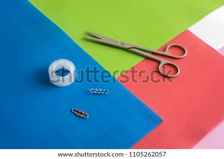 On colorful sheets of paper are scissors, paper clips, tape.