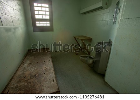 Interior of solitary confinement cell with metal bed, desk and toilet in old prison. Royalty-Free Stock Photo #1105276481