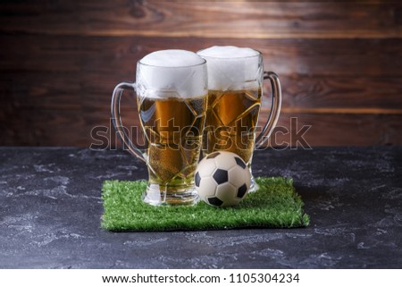 Photo of two beer mugs, green grass with soccer ball