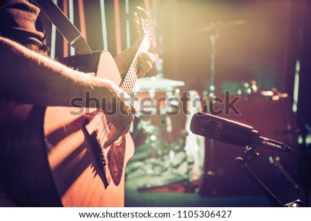 The Studio microphone records an acoustic guitar close-up, in a recording Studio or concert hall, with a drum set on a background in out-of-focus mode. Beautiful blurred background of colored lanterns