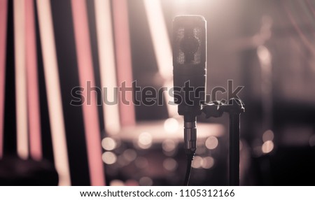 Microphone in recording Studio or concert hall close-up, with drum set on background out of focus. Beautiful blurred background of colored lanterns. Musical concept in vintage style.