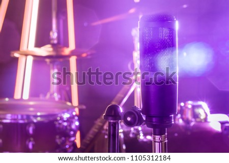 The microphone in a recording Studio or a concert hall close up of drum kit and an acoustic guitar in the background. Beautiful blurred background of colored lanterns. Musical concept.