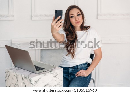 A portrait of a pretty shining girl with smooth even skin that sits in a cafe and makes selfie on her smartphone. Freelancer came to work in a restaurant and a cup of coffee.