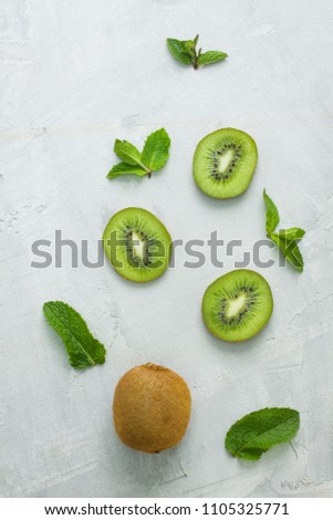 Fresh kiwi whole fruit and three kiwi slices with mint leaves on grey concrete background diagonally. Creative layout, food concept, flat lay, top view, vertical orientation.