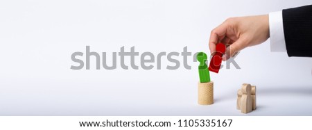 The man's hand of a businessman in a business suit holds a wooden figure of a man in his hand and moves another figure from his post. The concept of firing an employee, the replacement of staff Banner