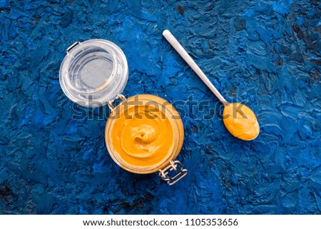 Nut butter in glass jar and spoon with butter on blue background top view