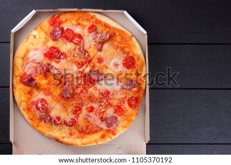 Pizza on a black wooden background, Italian pizza with tomatoes, bacon, sausages and cheese, fast food, festive food on a dark background, copy space