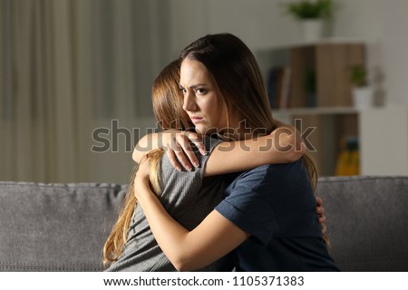 Angry woman hugging a friend sitting on a couch in the living room at home Royalty-Free Stock Photo #1105371383