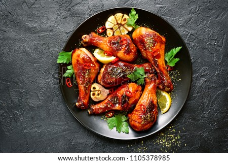 Roasted spicy chicken legs on a plate over black slate,stone or concrete background.Top view with copy space. Royalty-Free Stock Photo #1105378985