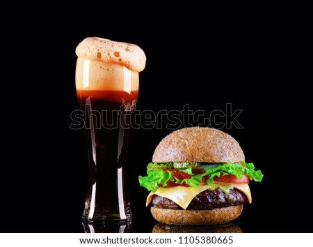 Close-up of delicious fresh home made burger with lettuce, cheese, onion, tomato and cola drink or dark beer with ice on black background