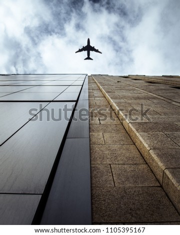 A plane passing over two contrasting buildings.