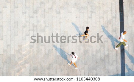 people walk on across the pedestrian concrete landscape with black silhouette shadow on ground (top aerial view)