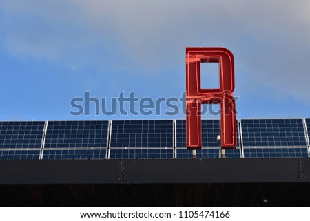 Red fluorescent tube sign letter on roof covered with solar panels.