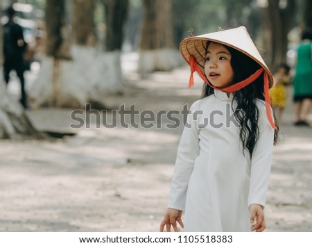 little girl in traditional costume Vietnam stood on the road with beautiful trees at sunset in Hanoi, Vietnam
