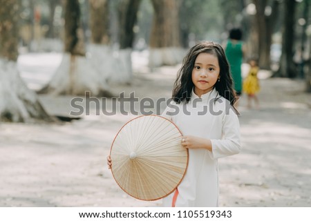 little girl in traditional costume Vietnam stood on the road with beautiful trees at sunset in Hanoi, Vietnam.