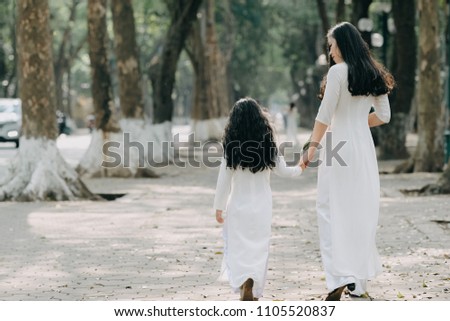the girl and mother in traditional Vietnamese costume stand on the road with beautiful trees at sunset in Hanoi, Vietnam.