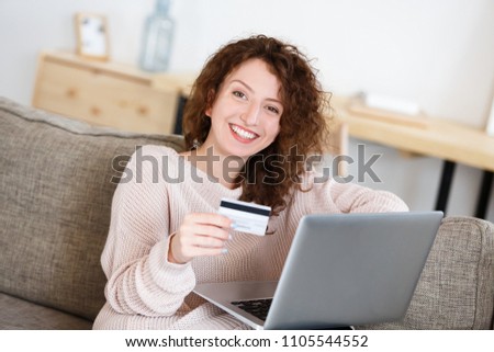 Happy and joyful redhead woman looking at camera with happy expression, hold in hand credit card, making transaction using laptop pc. Online shopping. People, business and finances concept.
