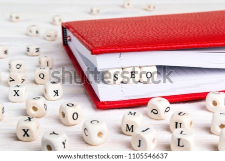 Word SEO written in wooden blocks in red notebook on white wooden table. Wooden abc.