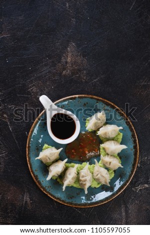 Turquoise plate with boiled wonton dumplings and dipping sauces, vertical shot over dark brown stone surface, copy space, vertical shot