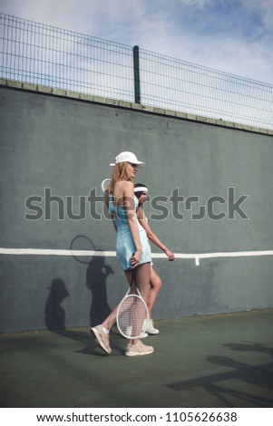 Portrait of two young Caucasian teen models wearing fashionable tennis dress, walking on a hardcourt during tennis practice, summer sunny day outdoors. Fashion portrait shoot